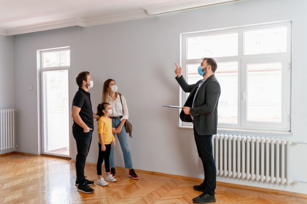 Confident male real estate agent gestures toward a beautiful view out the window of a new home. Interested potential homeowners attentively listen to the real estate agent.