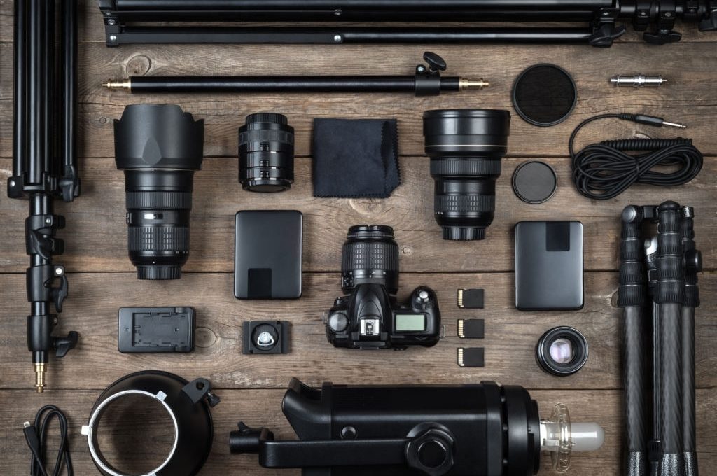 Set of the camera and photography equipment (lens, tripod, filter, flash, memory card, hard desk, reflector) on wood desk. Professional photographer accessories background.