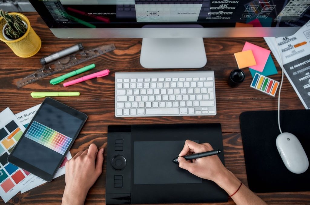 Top view of a designer using graphic tablet and working with computer while sitting at his workplace in the office. Top view of a workplace with graphic tablet, keyboard and computer.